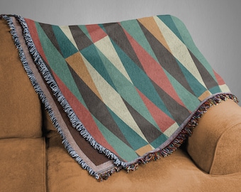 May include: A woven throw blanket with a geometric pattern in shades of brown, teal, cream, and red. The blanket has a fringe border and is draped over a brown couch.
