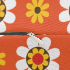 May include: Close-up of a zipper on a pillow with a bright orange background and a white and yellow daisy pattern.