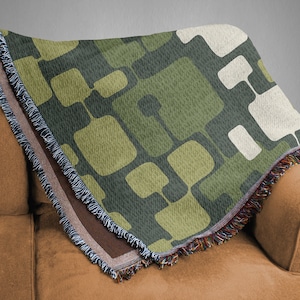 May include: A green, brown, and white woven throw blanket with a geometric pattern. The blanket has a fringe border and is draped over a brown couch.