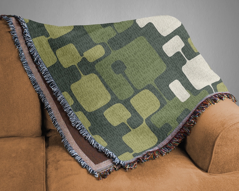 May include: A green, brown, and white woven throw blanket with a geometric pattern. The blanket has a fringe border and is draped over a brown couch.