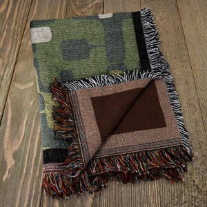 May include: A green and brown camouflage patterned woven throw blanket with a brown fabric backing and fringe trim.