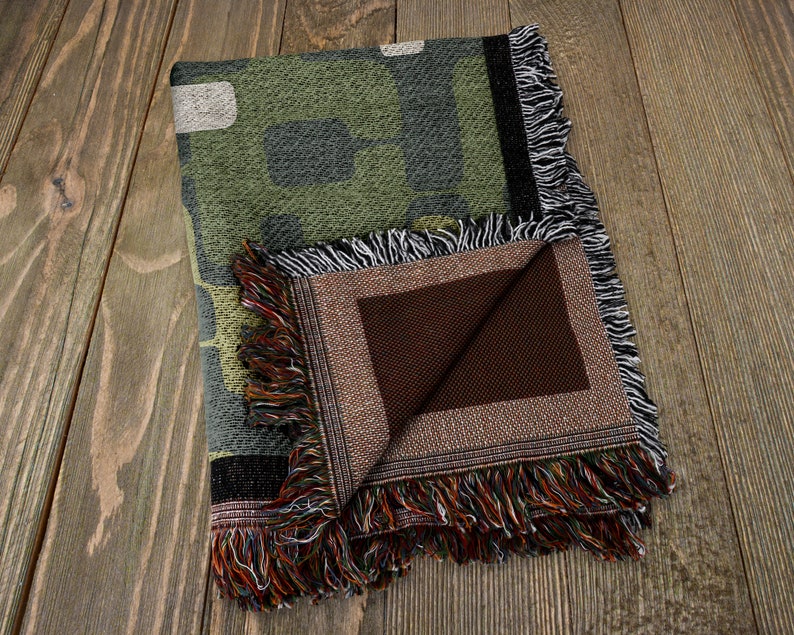 May include: A green and brown camouflage patterned woven throw blanket with a brown fabric backing and fringe trim.