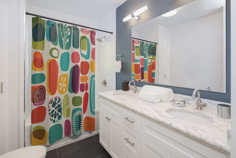 Pode incluir: Um banheiro branco com uma cortina de chuveiro que apresenta um padr&atilde;o abstrato colorido de c&iacute;rculos, ovais e redemoinhos. A cortina de chuveiro &eacute; feita de tecido e tem um fundo branco. O banheiro tamb&eacute;m tem uma pia branca com uma bancada de m&aacute;rmore e duas pias. H&aacute; uma toalha branca na bancada.