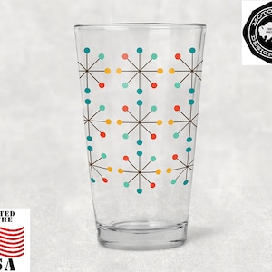 May include: A clear glass drinking glass with a mid-century modern geometric pattern in shades of teal, orange, yellow, and brown. The glass has a rounded bottom and a straight top.