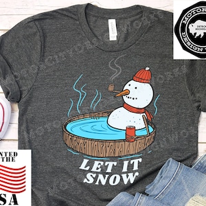 Op de afbeelding: Een donkergrijs T-shirt met een cartoon-sneeuwpop in een jacuzzi met de tekst "Let It Snow".
