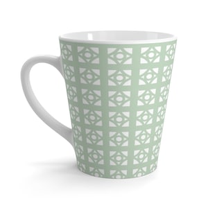 May include: A tall, white ceramic mug with a sage green geometric pattern. The pattern is a repeating design of squares with circles inside.