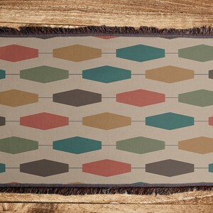 Pu&ograve; includere: Una coperta tessuta con un motivo geometrico di esagoni marroni, rossi, verdi e dorati su uno sfondo beige.