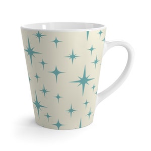 May include: A tall, white ceramic mug with a teal star pattern. The mug has a handle and is perfect for coffee or tea.