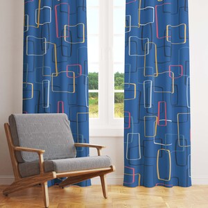 May include: Blue curtains with a mid-century modern design. The curtains feature a repeating pattern of rectangular shapes in white, yellow, pink, and gray, outlined in black. A gray armchair with wooden arms sits in front of the window.