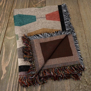 Pu&ograve; includere: Una coperta in tessuto tessuta piegata con un motivo geometrico in tonalit&agrave; di marrone, arancione, verde acqua e rosso. La coperta ha un bordo a frangia ed &egrave; realizzata in un tessuto morbido e testurizzato.