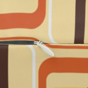 K&ouml;nnte beinhalten: Nahaufnahme eines Rei&szlig;verschlusses an einem Kissen mit einem Retro-Geometrie-Muster in Braun-, Orange- und Wei&szlig;t&ouml;nen.