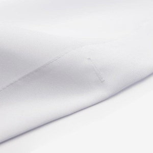 Pode incluir: Close-up de um tecido branco com uma textura sutil e uma &uacute;nica costura que atravessa a superf&iacute;cie diagonalmente.