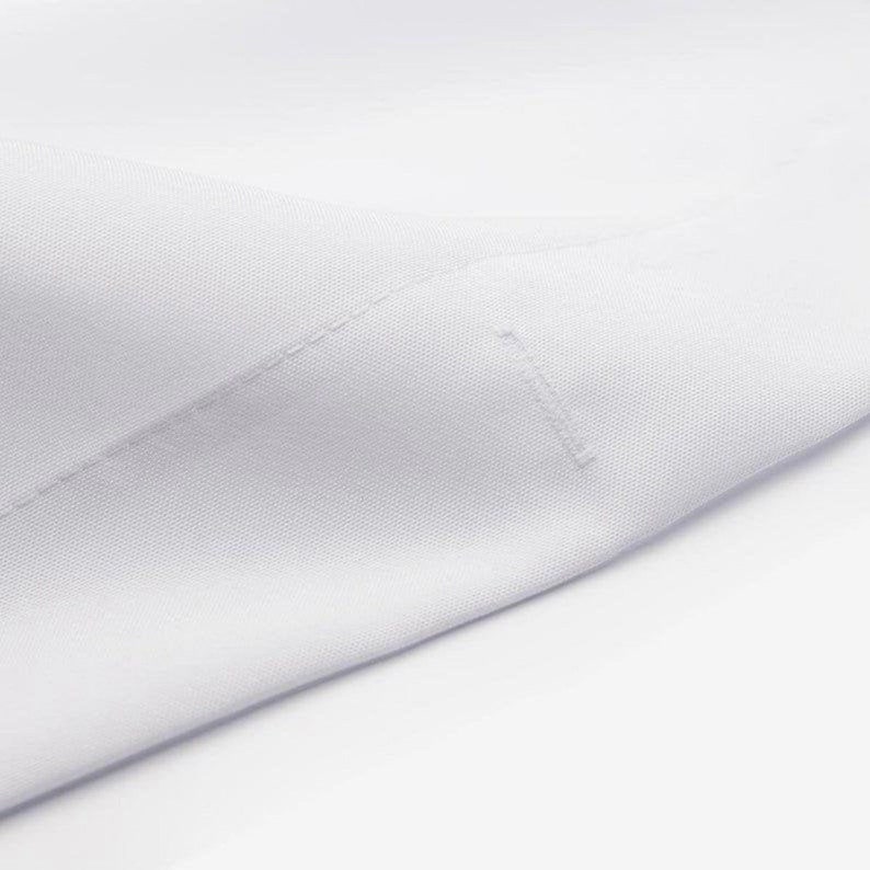 Pode incluir: Close-up de um tecido branco com uma textura sutil e uma &uacute;nica costura que atravessa a superf&iacute;cie diagonalmente.