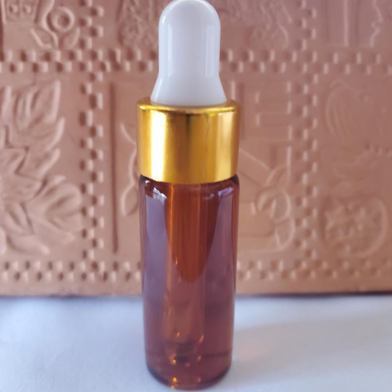 May include: A small, amber-colored glass bottle with a gold-colored cap and a white dropper. The bottle is filled with a liquid. The product is likely for essential oils or cosmetic use.