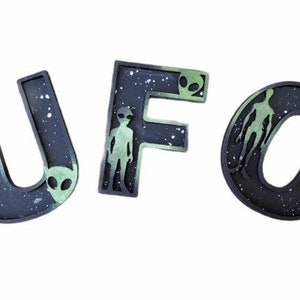 May include: Black and green letters spelling out the word "UFO" with a space-themed background and alien silhouettes.