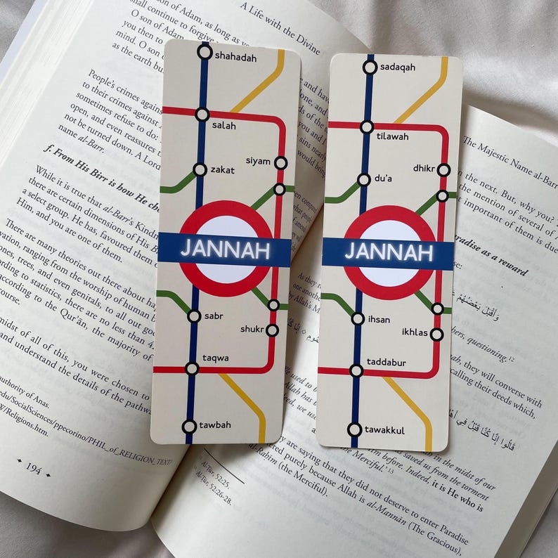 K&ouml;nnte beinhalten: Zwei rechteckige Lesezeichen mit U-Bahn-Kartendesign. Das Design zeigt einen roten Kreis mit dem Wort "JANNAH" in Blau, umgeben von farbigen Linien und arabischen W&ouml;rtern. Die Lesezeichen liegen auf einem offenen Buch.