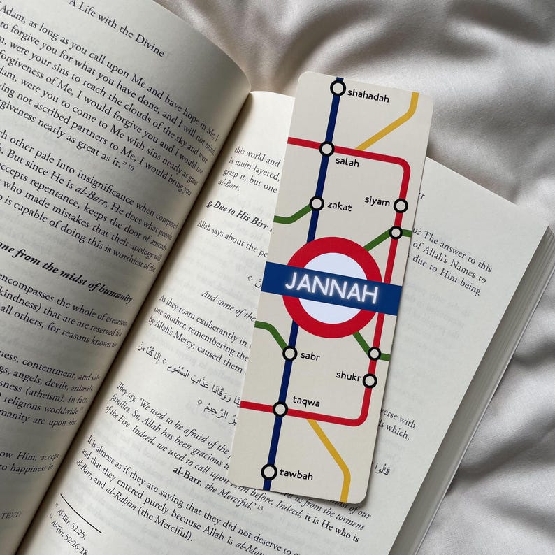 K&ouml;nnte beinhalten: Lesezeichen mit U-Bahn-Kartendesign, mit dem Wort "JANNAH" in einem roten Kreis. Das Lesezeichen hat farbige Linien und Etiketten wie "salah" und "zakat". Es liegt auf den Seiten eines offenen Buches.