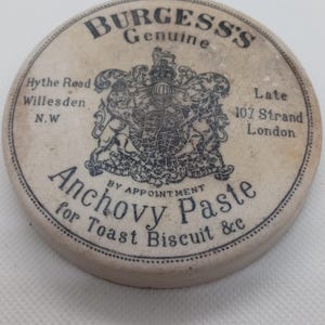 May include: A circular, cream-coloured ceramic lid featuring black text and a detailed crest. The text reads "BURGESS'S Genuine" and "Anchovy Paste for Toast Biscuit &c." Addresses in London and Willesden are also visible.