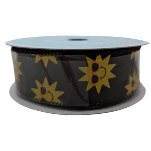 May include: A spool of black ribbon featuring a repeating pattern of yellow suns wearing sunglasses. The ribbon is wrapped around a white cardboard core and is partially covered in clear plastic.