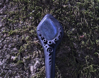 May include: A black wooden hair stick with a decorative top featuring a blue gemstone. The stick is adorned with intricate carvings and circles.