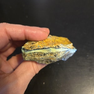 May include: A rough, irregular shaped piece of yellow, green, and black opal with a layered pattern.