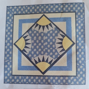 May include: A blue and yellow geometric pattern quilt block with a white background. The block is surrounded by a blue border with a white polka dot pattern.