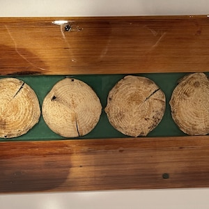 Może przedstawiać: Drewniana taca do serwowania z zielonym wkładką z żywicy i czterema drewnianymi plastrami. Taca ma dwa czarne metalowe uchwyty.