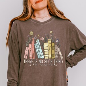 May include: Espresso-colored long-sleeve shirt with a graphic of colorful books and flowers. The text "THERE IS NO SUCH THING as too many books" is printed below the books. The shirt is a relaxed fit.