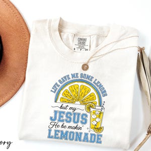 A white t-shirt with a graphic design and text, along with a brown hat and a plant, all placed on a white background.