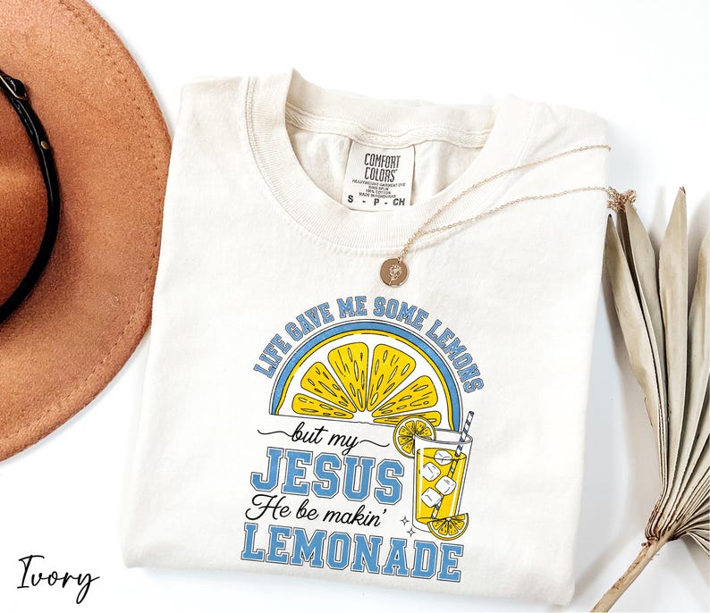 A white t-shirt with a graphic design and text, along with a brown hat and a plant, all placed on a white background.