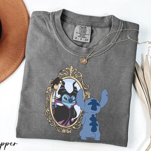 A gray t-shirt with a graphic design featuring a character from the Disney movie Lilo and Stitch, along with a mirror and a necklace.