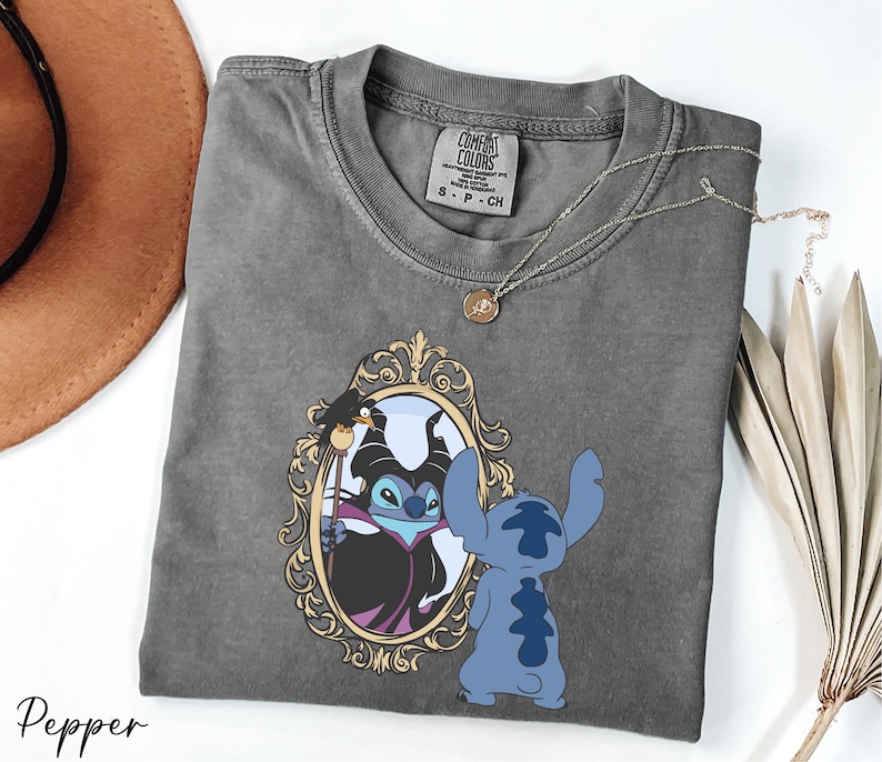 A gray t-shirt with a graphic design featuring a character from the Disney movie Lilo and Stitch, along with a mirror and a necklace.
