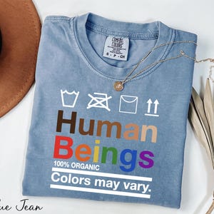 May include: A blue t-shirt with the words "Human Beings" in rainbow colors and the text "100% Organic Colors may vary."  The shirt has a care label with washing instructions.