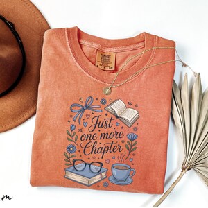 a red t-shirt with a printed design, a brown hat, a necklace, a fan, and some books, all arranged on a white background.