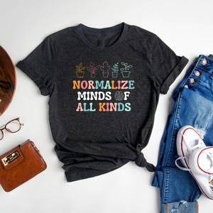 May include: A dark grey t-shirt with a graphic of potted plants and the text "Normalize Minds of All Kinds".
