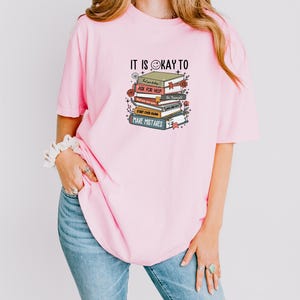 a woman wearing a pink shirt with a stack of books on it