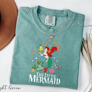 a green shirt with a little mermaid on it