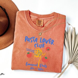 a t - shirt that says pasta lover club next to a hat