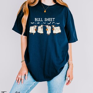 A woman wearing a navy blue t-shirt with a graphic design of three cows and the text "Bull Sheet" printed on it.
