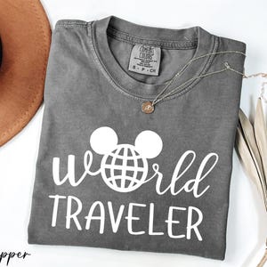a t - shirt that says world traveler next to a hat
