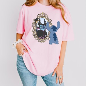 A woman wearing a pink t-shirt with a graphic of a character from the Disney movie "Stitch" and a mirror frame.