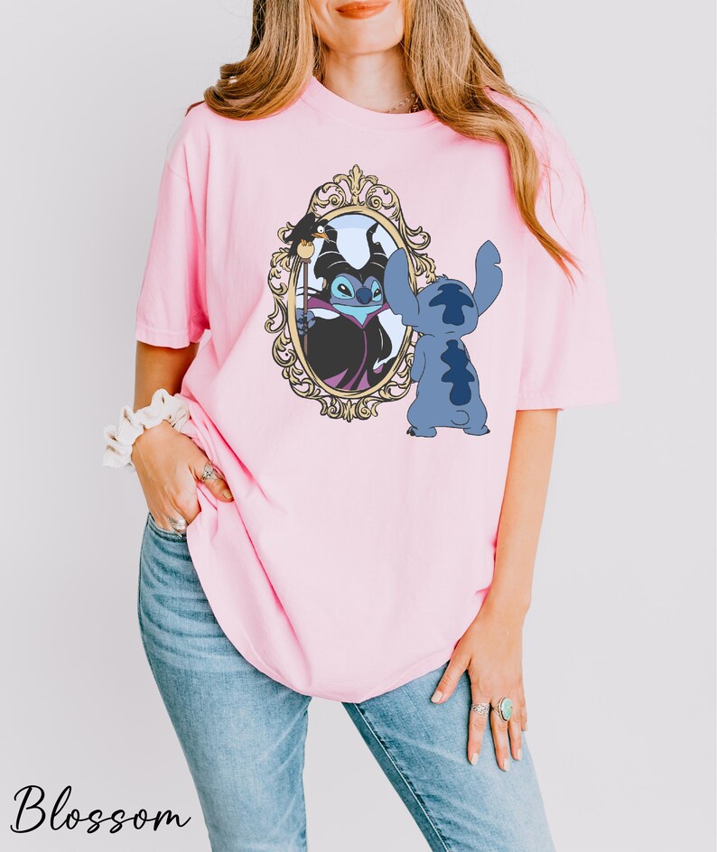 A woman wearing a pink t-shirt with a graphic of a character from the Disney movie "Stitch" and a mirror frame.