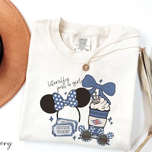 A white t-shirt with a graphic design featuring a cruise ticket, sunglasses, and a bow, along with a necklace and a hat.