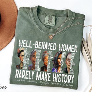 May include: A green t-shirt with a white graphic print featuring four women: Frida Kahlo, Rosa Parks, Maya Angelou, and Michelle Obama. The text reads "Well-behaved women rarely make history".