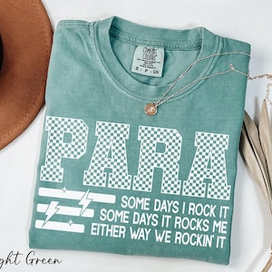 A light green t-shirt with a checkered pattern and text printed on it, along with a necklace and a brown hat.