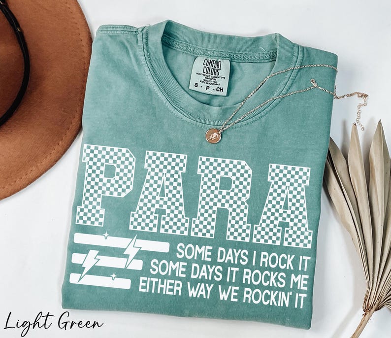 A light green t-shirt with a checkered pattern and text printed on it, along with a necklace and a brown hat.