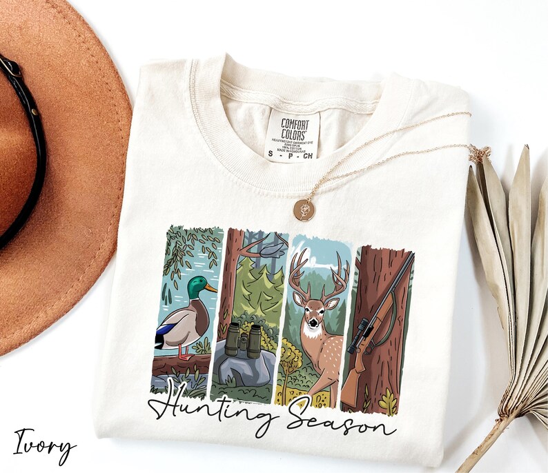 A white t-shirt with a graphic design depicting a deer, a bird, and a tree, along with the text "Hunting Season".