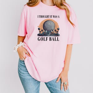 a woman wearing a pink shirt that says i thought it was a golf ball
