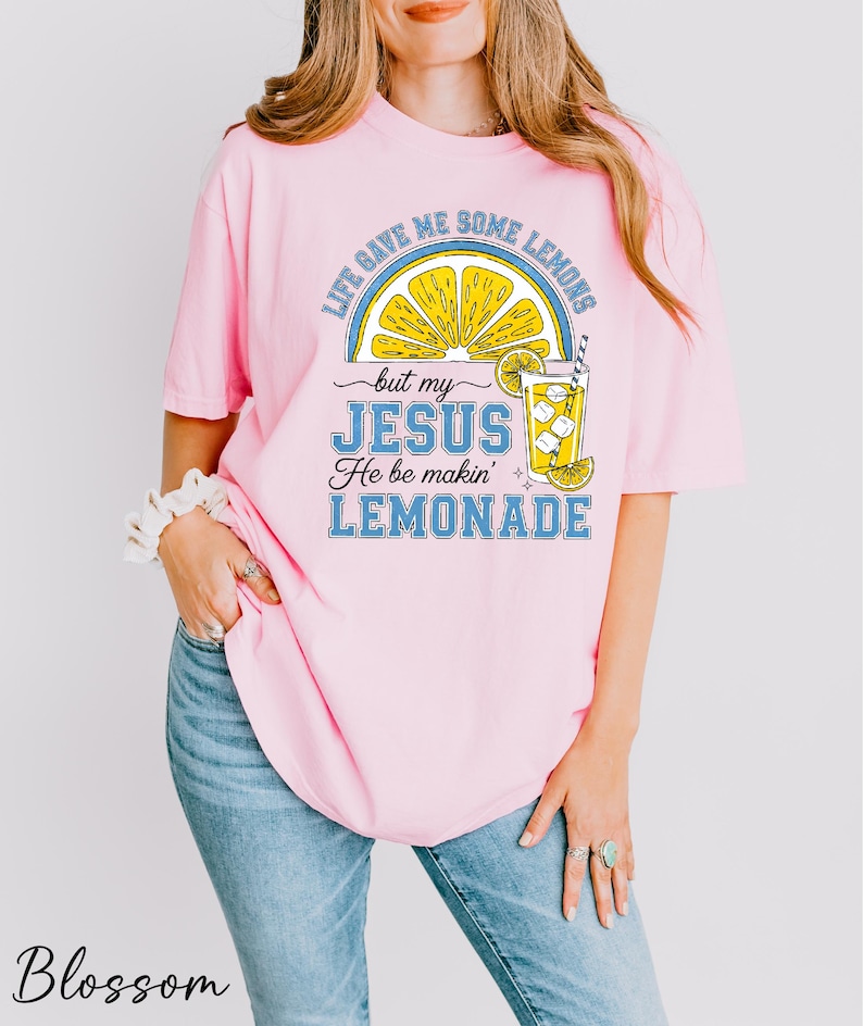A woman wearing a pink t-shirt with a graphic design of a lemonade glass and text that says "Life gives me some lemons but my JESUS He be makin' lemonade".