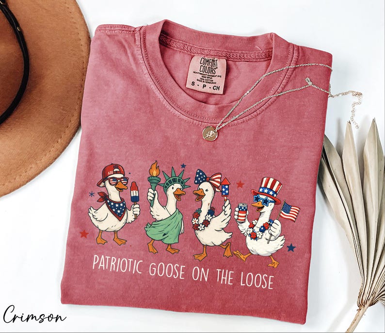 a red t-shirt with a patriotic goose design, along with a brown hat and some greenery.